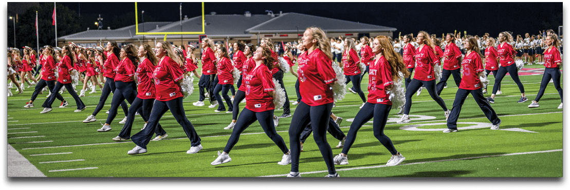 A large group of people wearing matching red shirts are performing a coordinated dance or exercise on a sports field at night. Description generated by AI