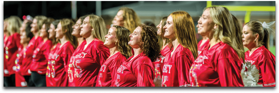 A group of people wearing matching red shirts stand in a line, facing the same direction with focused expressions. Description generated by AI