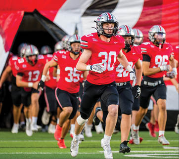 Three football players are standing on the field, one of them is smiling and wearing a black jersey with the number 55. AI generated content