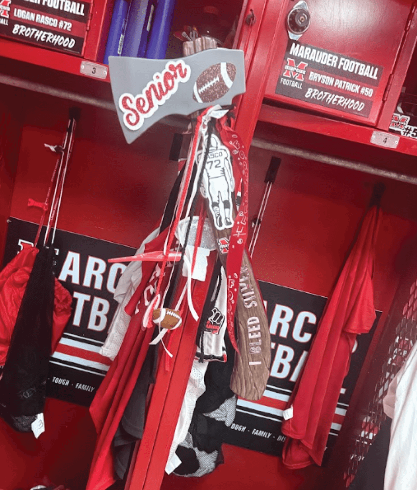 A red locker decorated with a white megaphone labeled “Senior" and various ribbons and accessories hanging from it, with football-themed signs and clothing inside. Description generated by AI