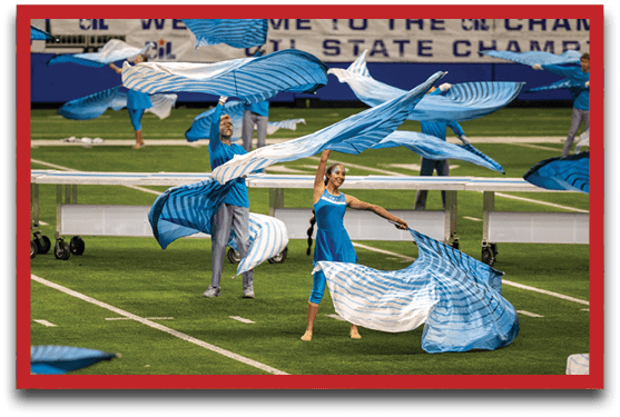 People in blue outfits are performing a coordinated flag routine on a green sports field. Description generated by AI