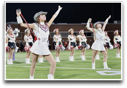 Adults dressed in coordinated white and red western-style outfits with hats perform a choreographed routine outdoors at night. Description generated by AI