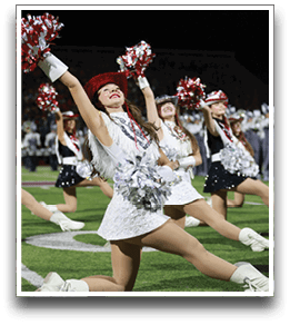 Adults dressed in sequined dance costumes and hats perform a synchronized routine on a football field at night. Description generated by AI
