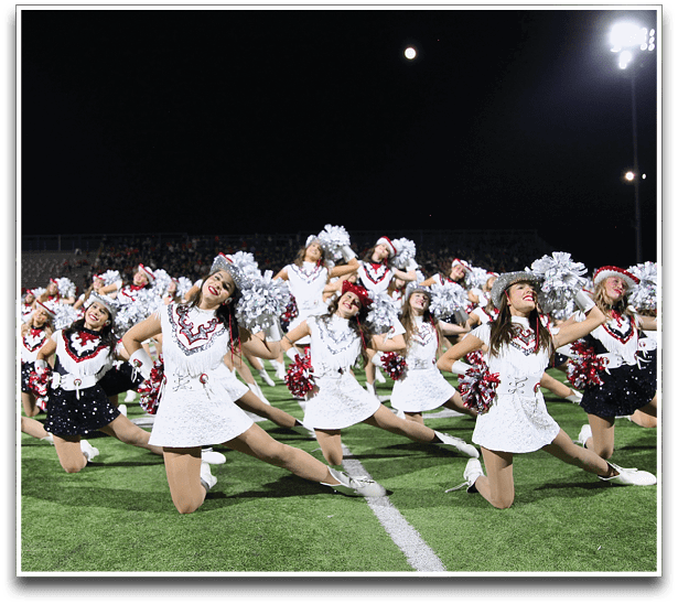 A group of people dressed in white uniforms with red and black accents are performing a synchronized dance routine on a football field at night under bright stadium lights. Description generated by AI