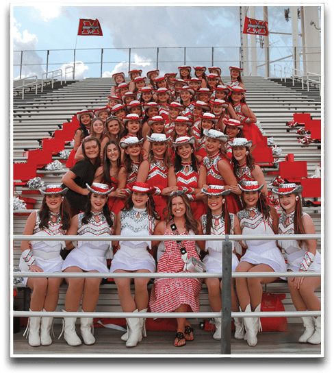 A group of people wearing matching red and white uniforms and hats are gathered closely together on bleachers with a large water tower and cloudy sky in the background. Description generated by AI