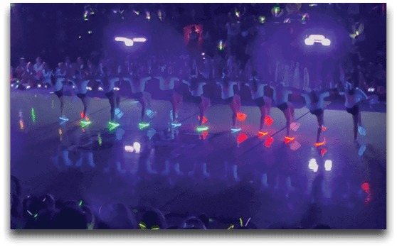 A large crowd of people is holding colorful glowing lights in a dark indoor setting. Description generated by AI