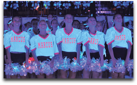 A group of people wearing matching white shirts with “MARCUS" written on them and holding shiny pom-poms are standing in a row under blue lighting. Description generated by AI