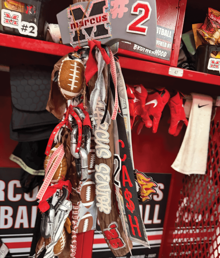 A sports locker shelf filled with football-themed items including gloves, a towel, a large foam finger with the number 2, and various ribbons and decorations. Description generated by AI