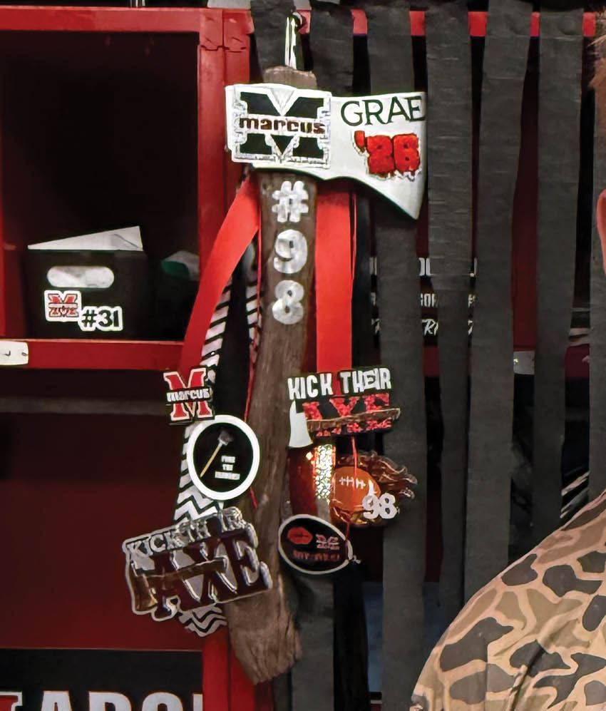 A close-up of a wooden chair with a white and red decorative sign attached to the backrest, featuring the text “GRAE" and "#98" along with other smaller text and symbols. Description generated by AI