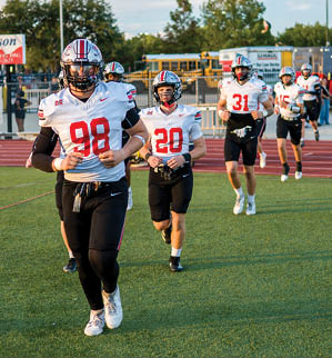 Three football players are standing on the field, one of them is smiling and wearing a black jersey with the number 55. AI generated content