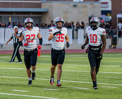 Three football players are standing on the field, one of them is smiling and wearing a black jersey with the number 55. AI generated content