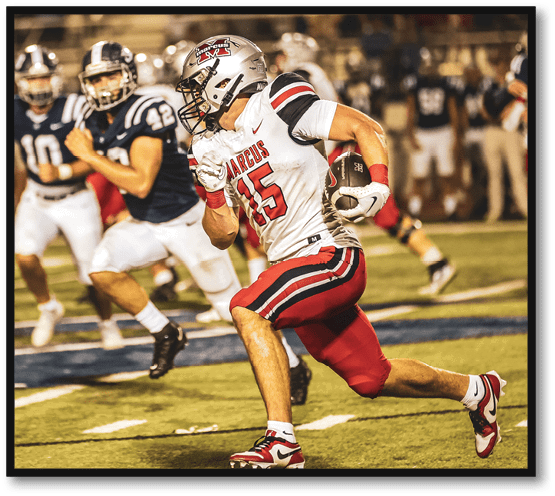 An adult wearing a white and red football uniform is running with the ball on a field while other players in dark blue uniforms chase behind. Description generated by AI