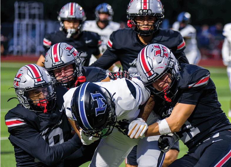 Several people in football uniforms are engaged in a tackle during a game on a grassy field. Description generated by AI