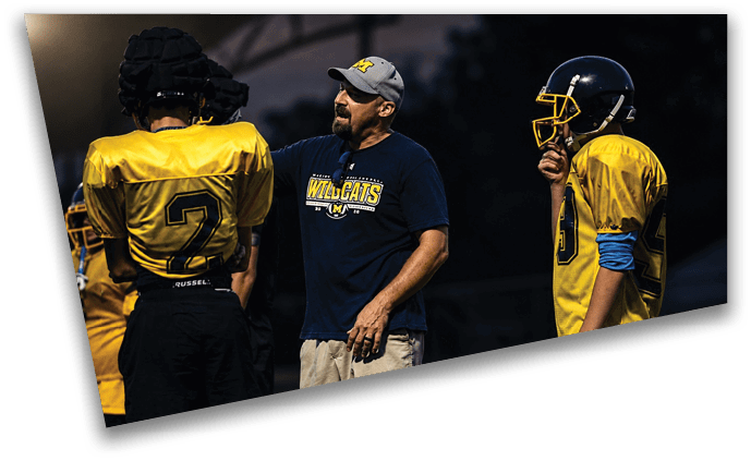 A man in a blue shirt is talking to two young men on a football field. AI generated content
