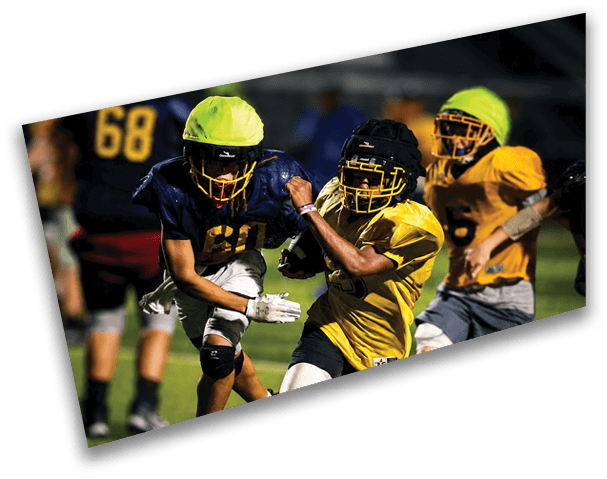 Two young men are playing football on a field. One boy is wearing a yellow jersey and the other is wearing a blue one. They are both running towards a football. AI generated content