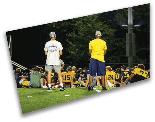 A group of people are sitting on a field, some of them wearing yellow shirts. AI generated content