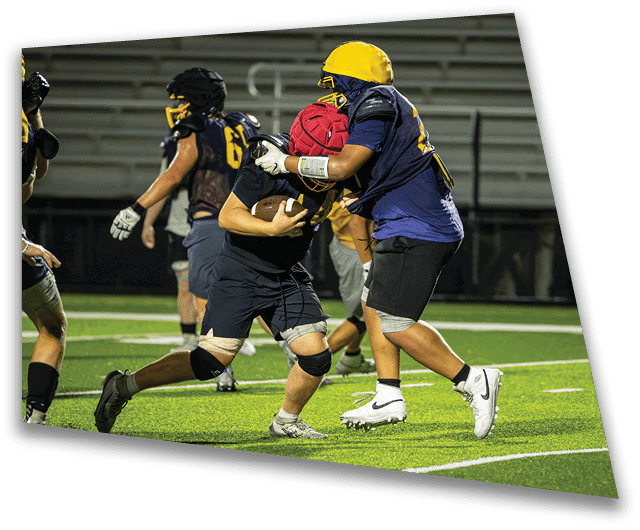 A group of football players on a field, one player is holding a football while another player is trying to take it from him. AI generated content
