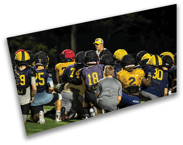 A football team is kneeling on the field, listening to their coach. AI generated content