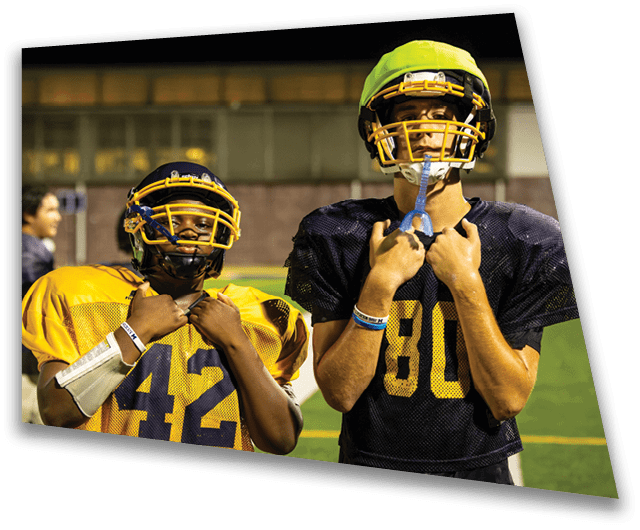Two football players wearing helmets and uniforms stand on a field. AI generated content