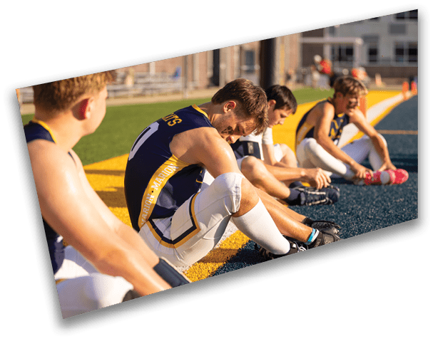 A group of young men are sitting on the ground in a football field. They are wearing uniforms and are resting their feet on the ground. AI generated content