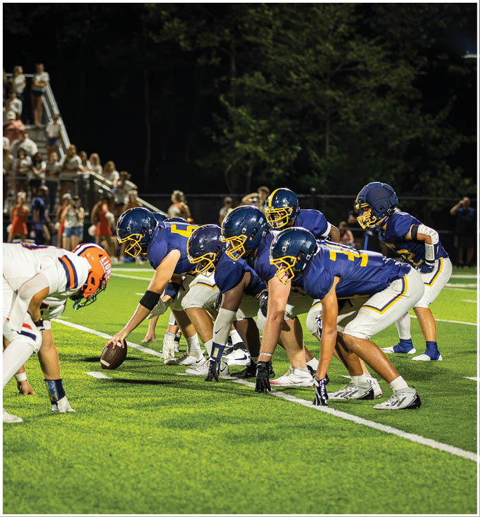A group of football players in blue and orange uniforms are lined up on a field, preparing for a play. AI generated content
