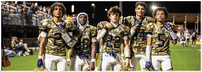 Five football players pose on the field, wearing camouflage uniforms and helmets. AI generated content