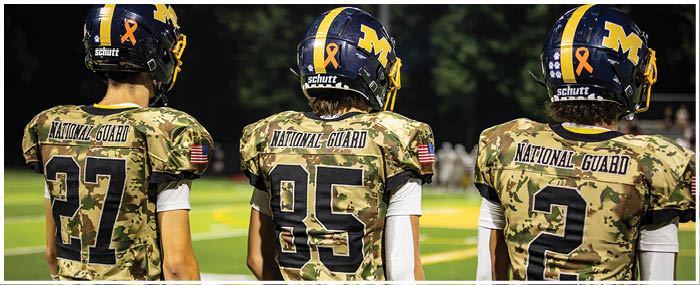Three football players wearing camouflage jerseys stand on a field. AI generated content