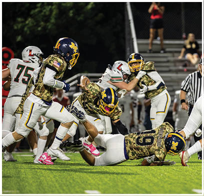 A group of football players are on the field, with one player falling to the ground. The referee is standing nearby, watching the play. AI generated content