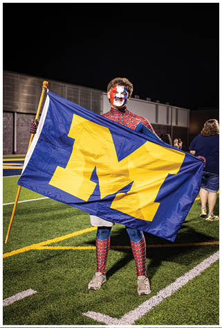 A man in a Michigan shirt and Spider-Man costume holds a flag. AI generated content