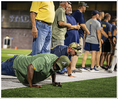 A man is doing a push-up on a football field while a crowd of people watch. AI generated content