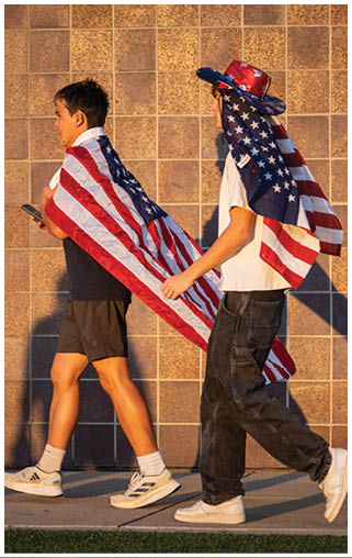 Two people walking with American flags on their backs. AI generated content