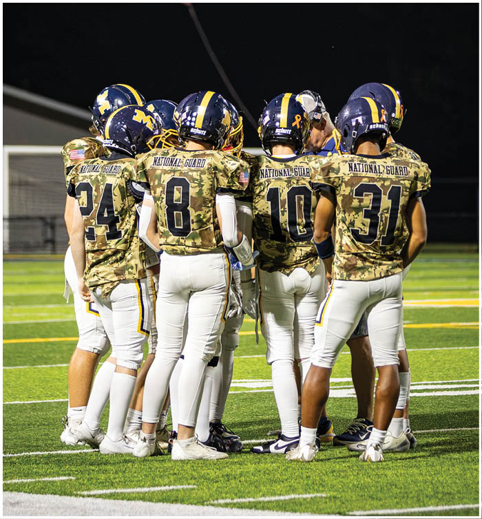 A group of football players huddle together on the field. AI generated content