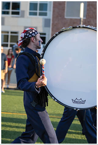 A man in a blue uniform is holding a drum while walking on a field. AI generated content