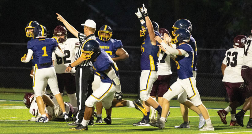 People in football uniforms are celebrating on a field at night while a referee stands nearby. Description generated by AI