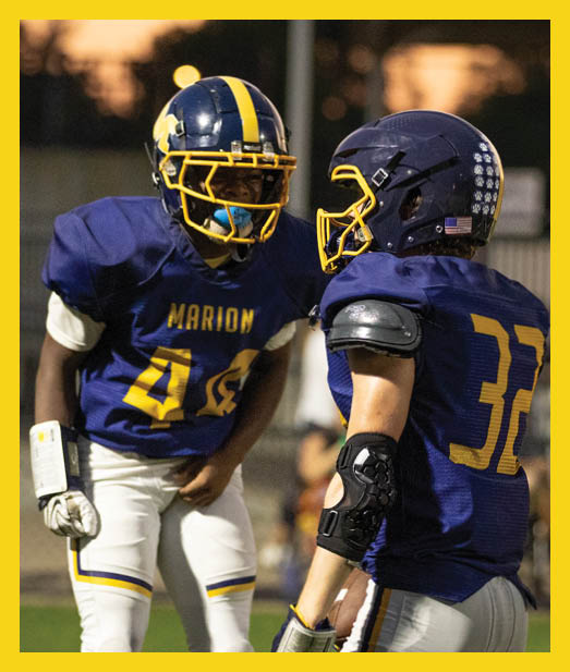 A person wearing a blue and yellow football uniform with the word Marion and the number 40 is standing on a field during a game. Description generated by AI