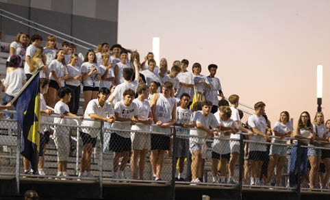 A group of people standing behind a chain-link fence wearing casual clothing and shorts. Description generated by AI
