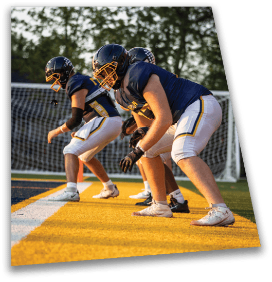 Three people in football uniforms and helmets are crouched in a ready stance on a field near a goal net. Description generated by AI
