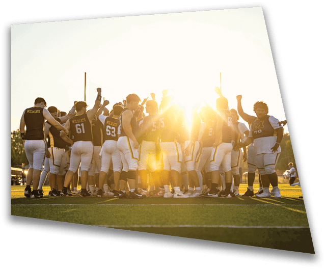 A group of people wearing football uniforms are gathered closely together on a field with the sun shining brightly behind them. Description generated by AI