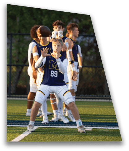 A person wearing a sports uniform with the number 89 is preparing to catch a ball on a football field while other players stand behind. Description generated by AI