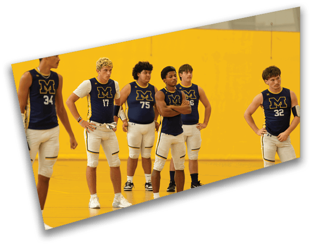 Six adults wearing matching sports uniforms with the letter M stand in a gymnasium with a yellow wall, appearing attentive and ready for an activity. Description generated by AI