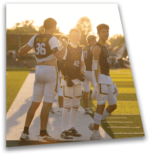 Two people wearing sports uniforms with numbers and standing on a field during sunset, one adjusting their shirt and the other smiling. Description generated by AI