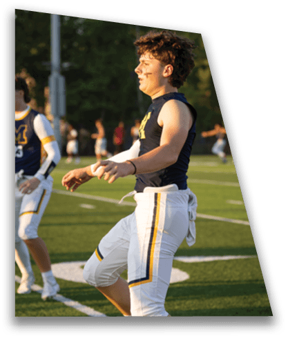 A person with curly hair wearing a sleeveless athletic shirt and face paint is standing outdoors on a sports field during daylight. Description generated by AI
