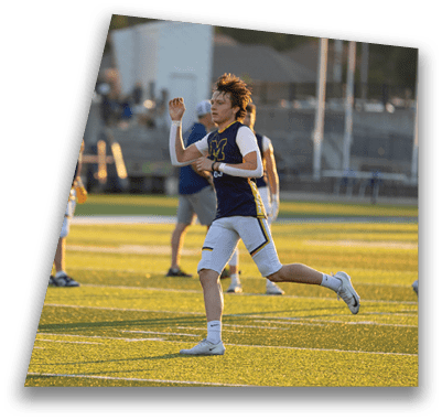 People wearing sports uniforms are running and standing on a sunlit artificial turf field. Description generated by AI