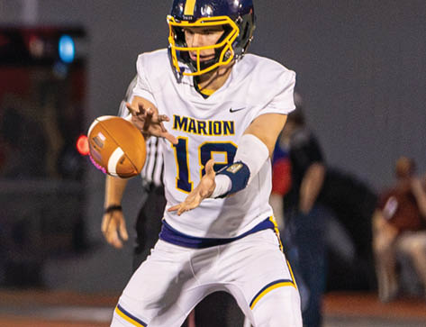 People in football uniforms are engaged in a play on a field with artificial turf and a large logo at the center. Description generated by AI