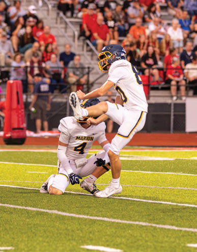 A group of people in football uniforms are on a field with one person kicking a ball held by another person while others watch. Description generated by AI
