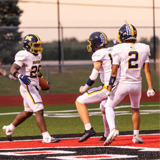 Three people in football uniforms are on a field with one person holding a football and the other two appearing to celebrate or interact near the end zone. Description generated by AI