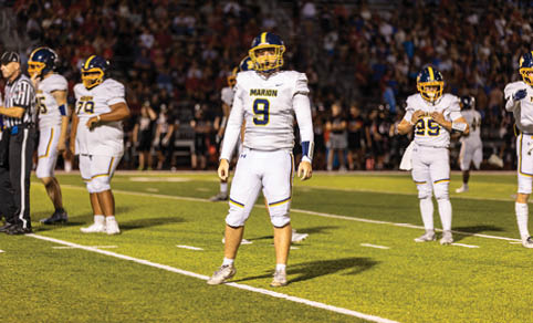 People in football uniforms stand on a field under bright lights with a crowd in the background. Description generated by AI