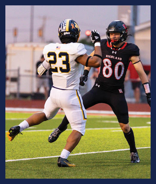 Two people in football uniforms are engaged in a play on a green field with one person wearing a black uniform and the other in a white uniform. Description generated by AI