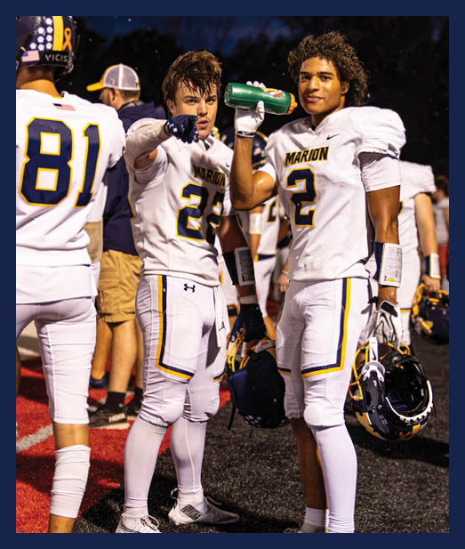 Two adults in matching navy blue cheerleading uniforms with white boots and bows perform with white pom-poms on a sports field. Description generated by AI