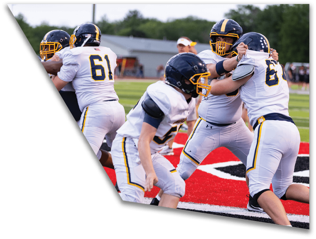 People wearing football uniforms and helmets are engaged in a physical play on a football field near the end zone. Description generated by AI
